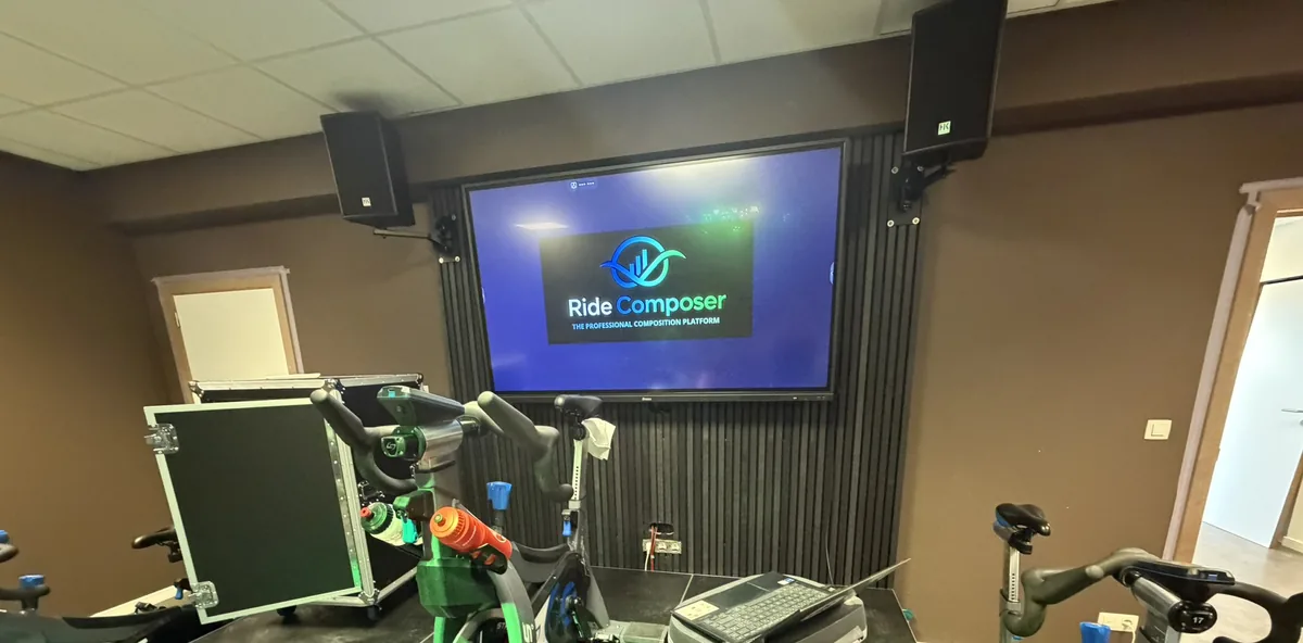 An indoor cycling studio with bikes facing a wall screen driven by RideComposer from a laptop